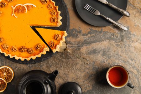 thanksgiving pumpkin pie near cup of tea and black tableware with vintage cutlery on stone surface