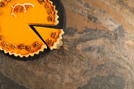 cake spatula near thanksgiving pie garnished with orange slices and walnuts on textured stone table