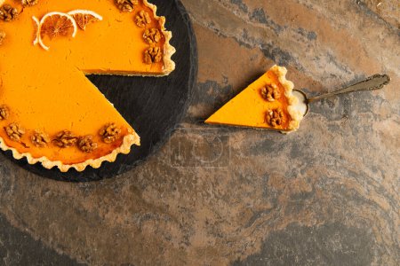 cake spatula with thanksgiving pie decorated with orange slices and walnuts on stone tabletop