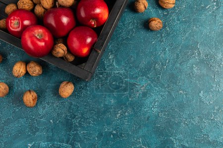 plateau en bois noir avec pommes rouges et noix sur surface texturée bleue, cadre d'action de grâces