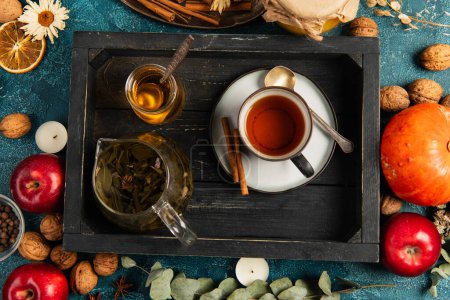 colorido ajuste de acción de gracias, bandeja de madera negra con té de hierbas y miel cerca de objetos de cosecha de otoño
