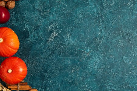 Photo for Ripe orange pumpkins near cinnamon sticks and apple on blue textured backdrop, thanksgiving setting - Royalty Free Image