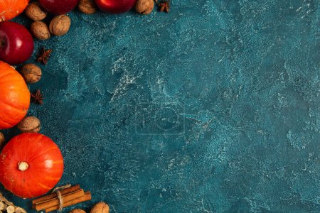 calabazas anaranjadas cerca de manzanas rojas y nueces sobre fondo texturizado azul, concepto de acción de gracias