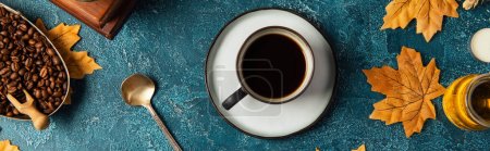 cup of black coffee near golden maple leaves on blue textured tabletop, thanksgiving concept, banner