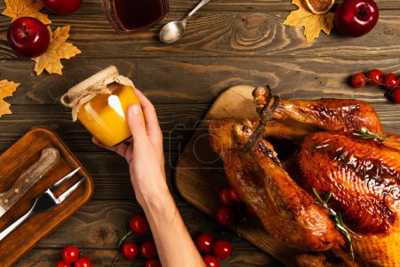 cropped view of man with jar of honey near thanksgiving turkey on wooden table with autumnal decor