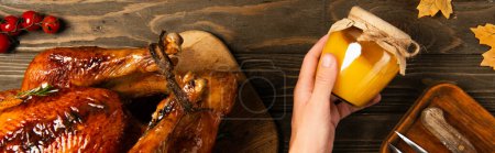 Foto de Cena de acción de gracias, mano masculina con tarro de miel cerca de pavo a la parrilla y tomates rojos cereza, pancarta - Imagen libre de derechos