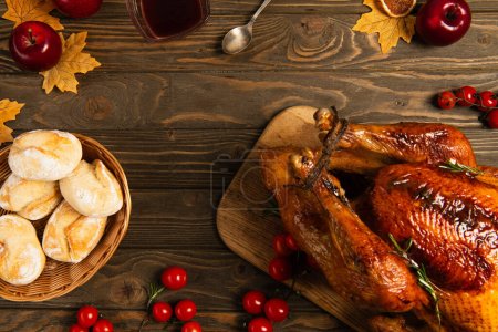Photo for Thanksgiving turkey and buns on wooden table with golden foliage and red cherry tomatoes with apples - Royalty Free Image