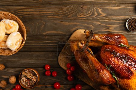 Photo for Freshly baked buns and spices with cherry tomatoes near roasted turkey on wooden table, thanksgiving - Royalty Free Image