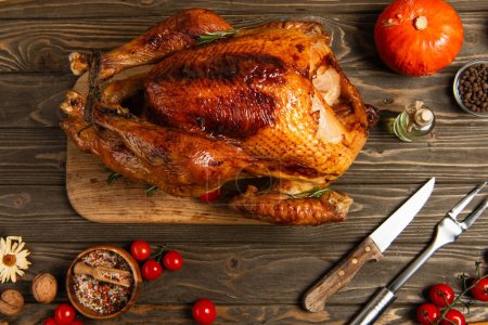 Photo for Delicious thanksgiving, roasted turkey near cherry tomatoes, spices and cutlery on wooden tabletop - Royalty Free Image