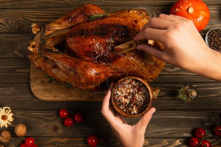 thanksgiving dinner, partial view of man seasoning turkey near cherry tomatoes on wooden table