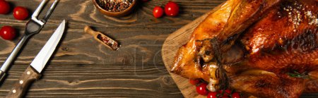 Photo for Roasted thanksgiving turkey near spices, cutlery and red cherry tomatoes on wooden tabletop, banner - Royalty Free Image