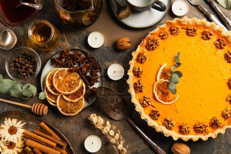 thanksgiving pumpkin pie with walnuts and orange slices near warm tea on decorated stone table