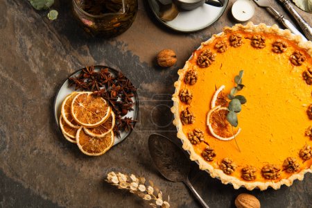 stone table with festive thanksgiving decor and delicious pumpkin pie with walnuts and orange slices