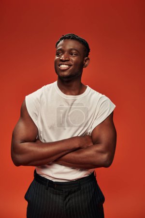 hombre americano africano deportivo feliz en camiseta blanca posando con los brazos cruzados y mirando hacia otro lado en rojo