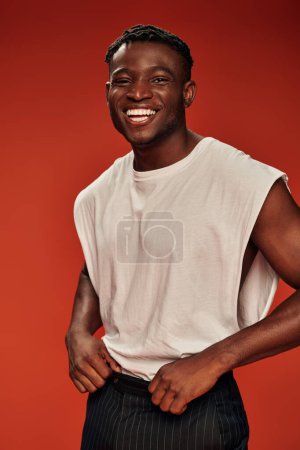 cheerful african american guy in trendy casual clothes looking at camera and laughing on red