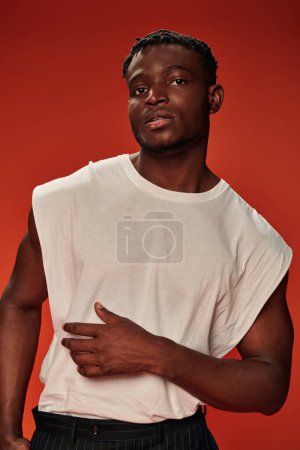 Foto de Carismático hombre afroamericano elegante en camiseta blanca mirando a la cámara en rojo, estilo moderno - Imagen libre de derechos