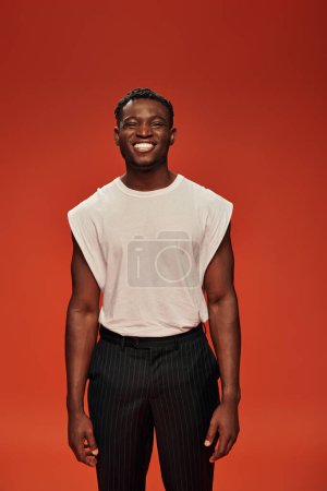 front view of pleased african american man in stylish casual clothes smiling at camera on red