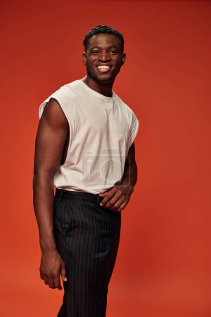 ravi homme afro-américain en vêtements de rue à la mode souriant à la caméra sur rouge, positivité