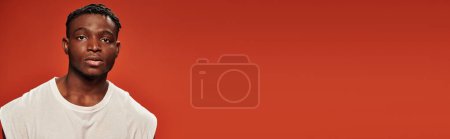Photo for Good-looking stylish african american male model in white tank top looking at camera on red, banner - Royalty Free Image