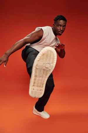 hot african american guy in striking pose with outstretched leg on red and orange backdrop