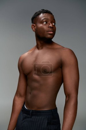 young and confident african american guy with shirtless muscular body looking away on grey backdrop