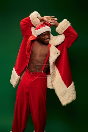 hot african american guy in christmas costume on shirtless body smiling and looking away on green