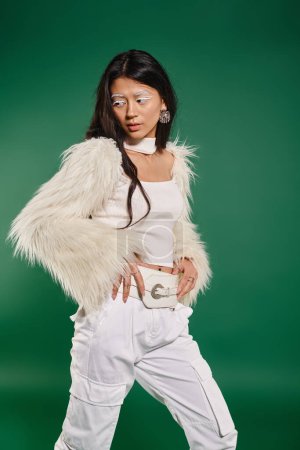 asian brunette woman in total white outfit and makeup posing on green backdrop, winter fashion