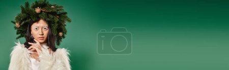 Photo for Banner of woman in faux fur jacket and natural wreath on head looking at camera on green backdrop - Royalty Free Image
