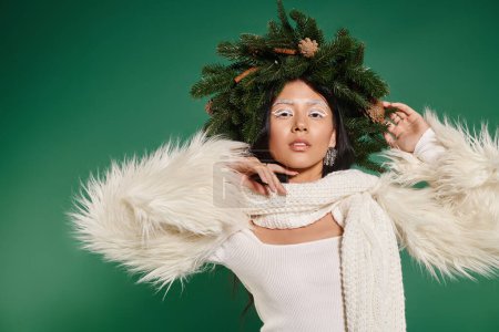 espíritu navideño, hermosa mujer asiática con maquillaje blanco y traje de moda posando en corona en verde