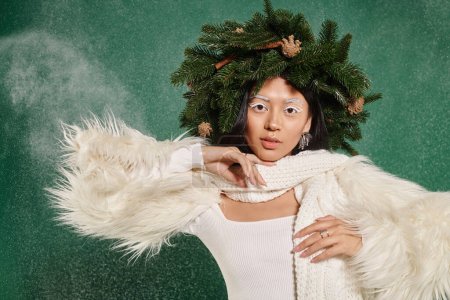 Téléchargez les photos : Temps d'hiver, belle femme avec maquillage blanc et tenue à la mode posant en couronne sous la neige tombante - en image libre de droit