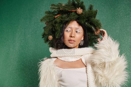 winter fashion, dreamy asian woman with natural wreath posing in white clothes under falling snow