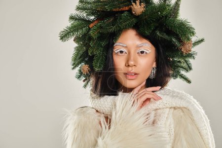 concepto de invierno, hermosa mujer con corona de pino natural posando en ropa blanca sobre fondo gris