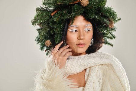 belleza de invierno, mujer atractiva con corona de pino natural posando en ropa blanca sobre fondo gris