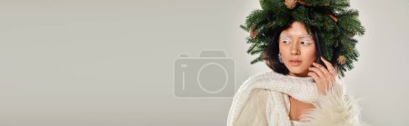 belleza de invierno, mujer atractiva con corona de pino natural posando en ropa blanca en gris, bandera