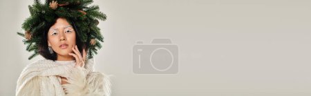 Winter-Schönheitsbanner, verführerische Frau mit Kiefernkranz posiert in weißen Kleidern vor grauem Hintergrund