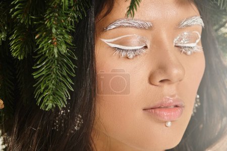winter beauty, close up of young woman with white eye makeup and beads on face posing in wreath tote bag #681548426