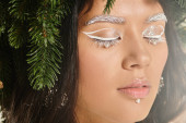 winter beauty, close up of young woman with white eye makeup and beads on face posing in wreath tote bag #681548426