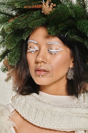 winter trends, close up of asian woman with white eye makeup and beads on face posing in wreath
