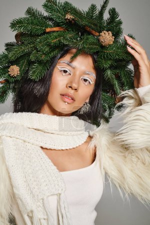Foto de Atractiva reina de invierno con maquillaje de ojos blancos y cuentas en la cara posando en corona sobre fondo gris - Imagen libre de derechos