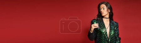 Téléchargez les photos : Brunette asiatique femme en veste verte avec des paillettes tenant des lunettes sur fond rouge, bannière - en image libre de droit