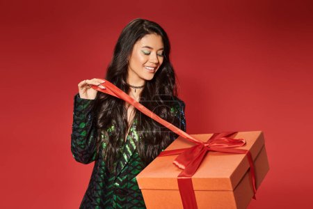 happy asian woman in green jacket with sequins pulling ribbon on gift box, Merry Christmas