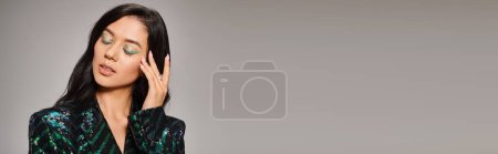 Téléchargez les photos : Attrayant asiatique femme en veste verte avec des paillettes et audacieux maquillage des yeux posant sur gris, bannière - en image libre de droit