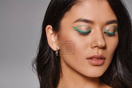 portrait of beautiful asian woman with brunette hair and shimmery eye makeup posing with closed eyes