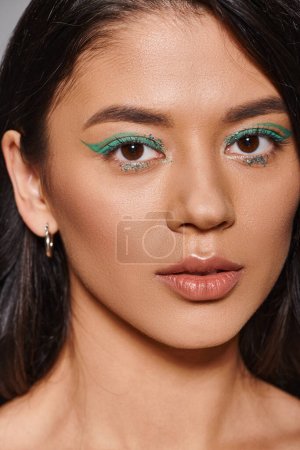Porträt der schönen asiatischen Frau mit brünetten Haaren und glänzenden Augen Make-up auf grauem Hintergrund