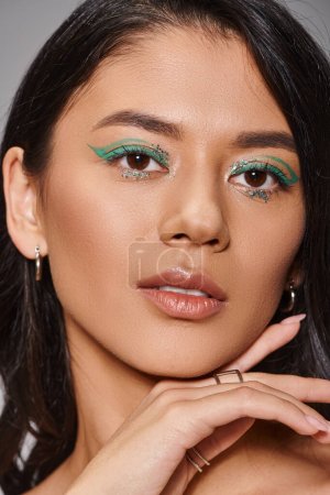 Porträt einer charmanten Asiatin mit brünetten Haaren und glänzendem Augen-Make-up auf grauem Hintergrund