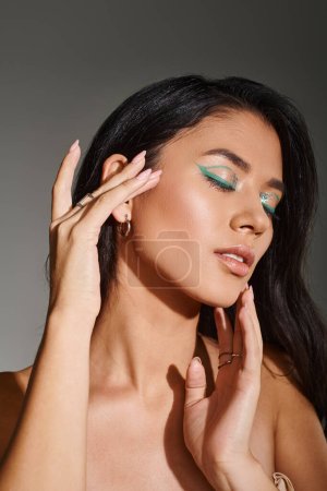 portrait of pretty asian woman with brunette hair and shimmery eye makeup posing on grey background