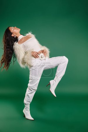 full length of stylish asian woman in white winter attire posing with closed eyes on green backdrop