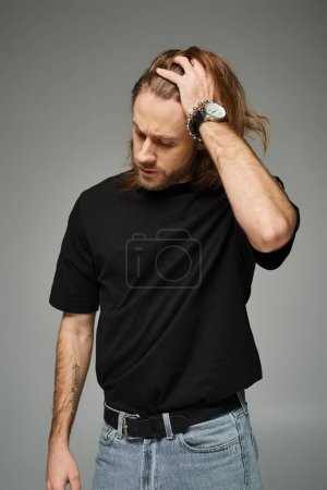 bärtiger, gutaussehender Mann in schwarzem T-Shirt und Jeans mit langen Haaren und grauem Hintergrund