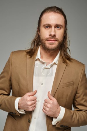 Photo for Good looking businessman with beard and long hair posing in blazer on grey backdrop, formal attire - Royalty Free Image