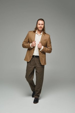 full length of businessman with beard and long hair posing on grey backdrop, formal attire
